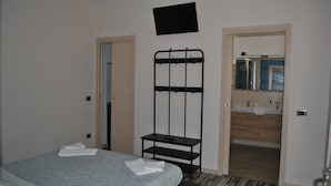 A hotel room with a bed, a black TV mounted on the wall, and a bathroom visible through an open door. - The Odeon Terrace (Catania)