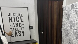 Ein Schlafzimmer mit einem Bett, einem Schreibtisch, einem Sessel, einer Wand mit einem Motivationsspruch, einer Tür und einer Wand mit Muster.