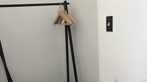 Ein Eckzimmer mit einem schwarzen Metallgestell, einem hölzernen Kleiderbügel und einem schwarzen Babybett.
