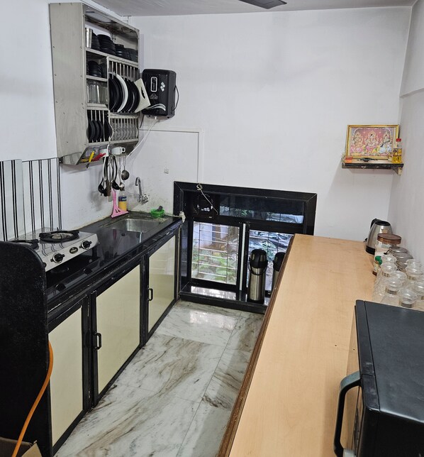 A compact kitchen with a gas stove, a microwave, and a sink. There is a window with a view of greenery outside. - Astha Kandivali Service Apt (Mumbai)
