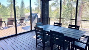 A covered outdoor deck with a table and chairs, large windows, and a view of trees and a grill. - Modern Pines-6 Bedroom, 5.5 Bath. 4 Master Suites! (Lead)