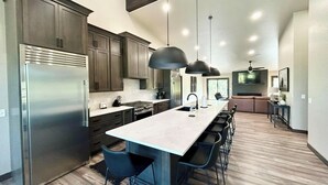 A modern kitchen with a central island, bar stools, and a dining area with a sofa. - Modern Pines-6 Bedroom, 5.5 Bath. 4 Master Suites! (Lead)