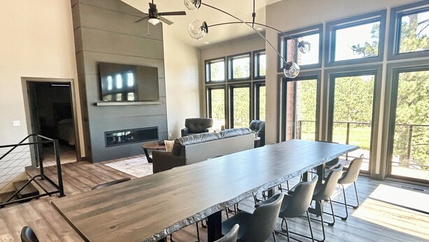 A spacious dining area with a long table and multiple chairs, a fireplace, and large windows offering a view of the outdoors. - Modern Pines-6 Bedroom, 5.5 Bath. 4 Master Suites! (Lead)