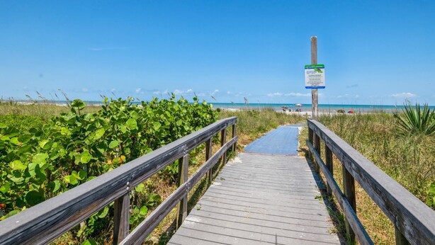A wooden boardwalk leading to a beach with a signpost in the distance.