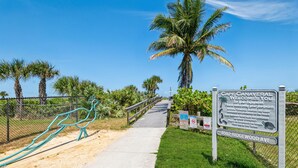 A pathway leading to a beach area with a signboard and a metal sculpture.