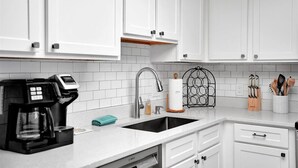 A modern kitchen with white cabinets, a stainless steel sink, a coffee maker, and a knife block.
