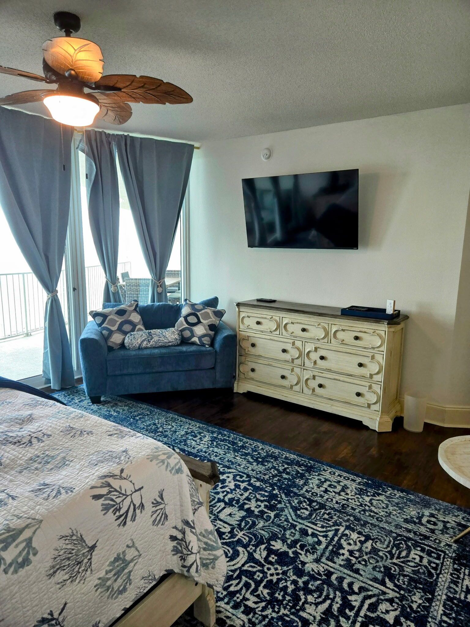 Une chambre à coucher comprenant un lit, une commode, un téléviseur et un ventilateur de plafond.