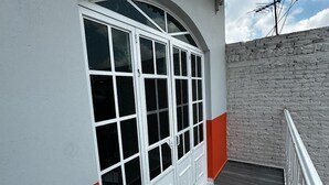 Een balkon met een witte en rode muur, een grijze vloer en een metalen hekwerk.