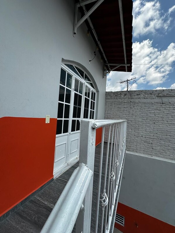 A building with a white and red facade, a metal railing, and a stone wall. - Privada Residencial 3 Luces B (Guadalajara)