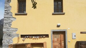 A yellow building with a stone wall, wooden door, and steps leading to a porch. - Rifugio Monte Zeus (Premia)