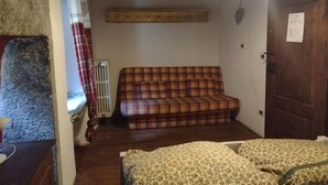 A room with a plaid sofa, a bed with patterned bedding, a wooden ceiling, and a door with a notice. - Rifugio Monte Zeus (Premia)