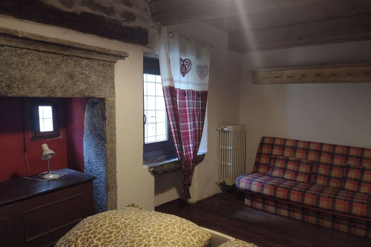 A room with a bed, a window with a heart-patterned curtain, a radiator, and a plaid sofa.
