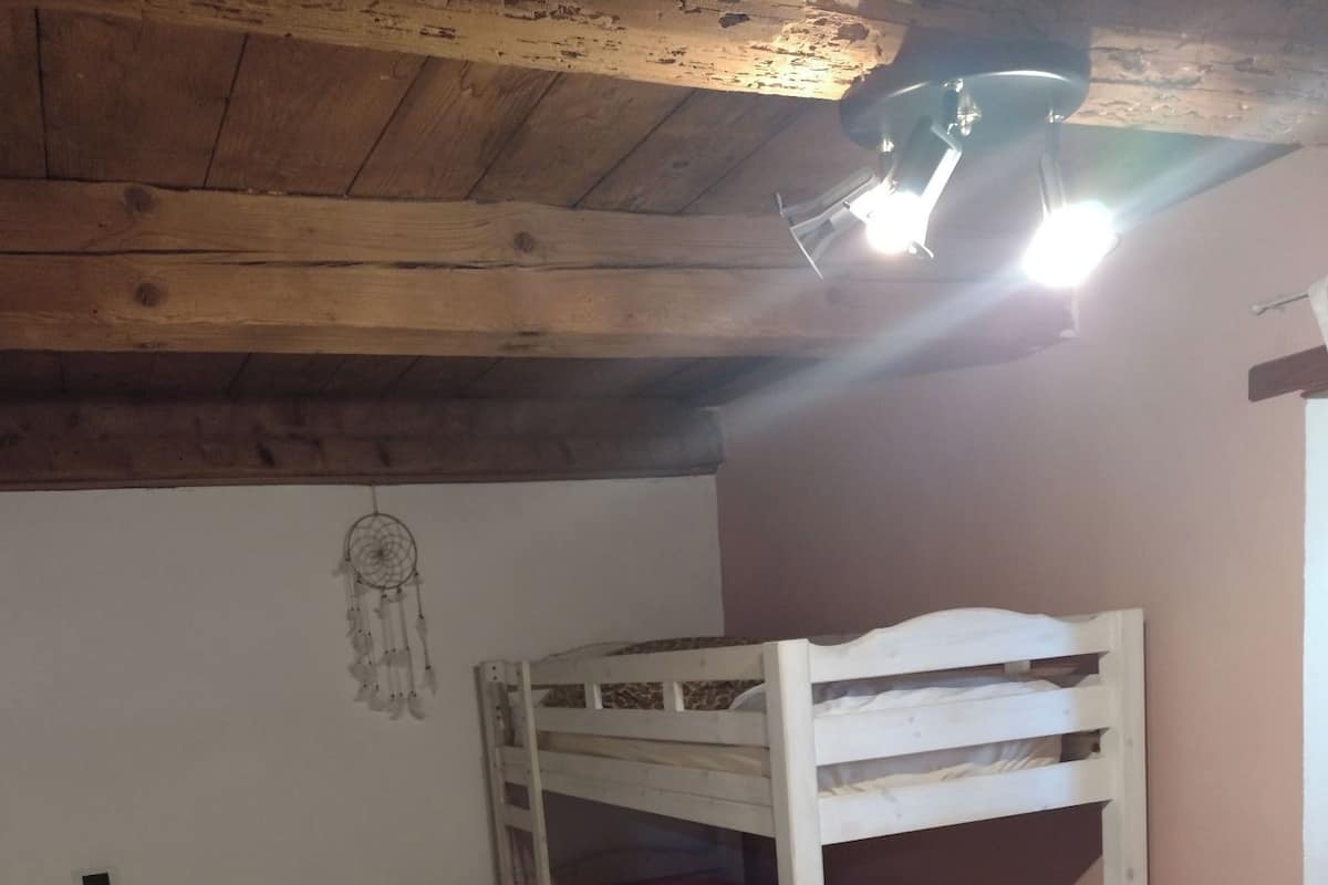 A bunk bed with a red chair, a desk with a lamp, and a dreamcatcher on the wall.