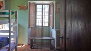 A room with bunk beds, a bench, a door, and a window with a view. - Rifugio Monte Zeus (Premia)