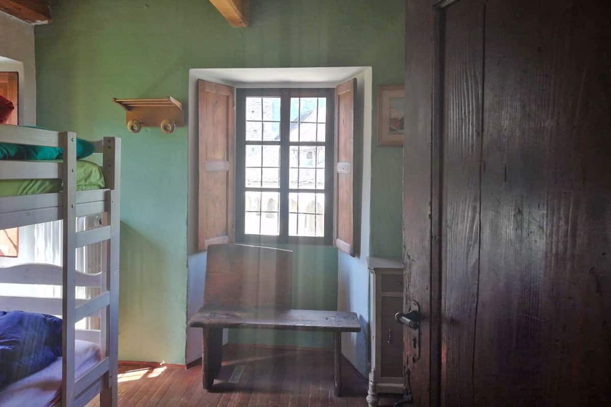 A room with bunk beds, a bench, a door, and a window with a view.