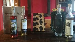 A selection of wine bottles on a wooden table with a red wall and a decorative panel in the background. - Rifugio Monte Zeus (Premia)