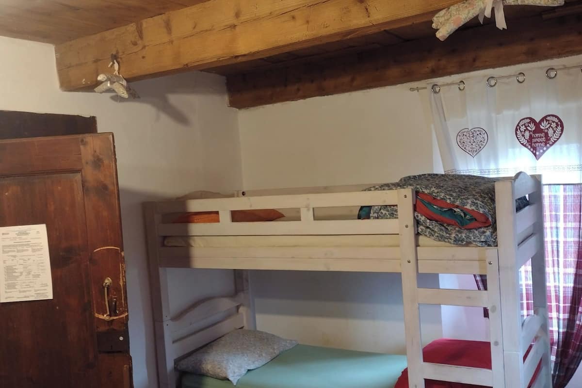 A bunk bed with a wooden ceiling, a door with a paper on it, and a window with heart-shaped curtains.