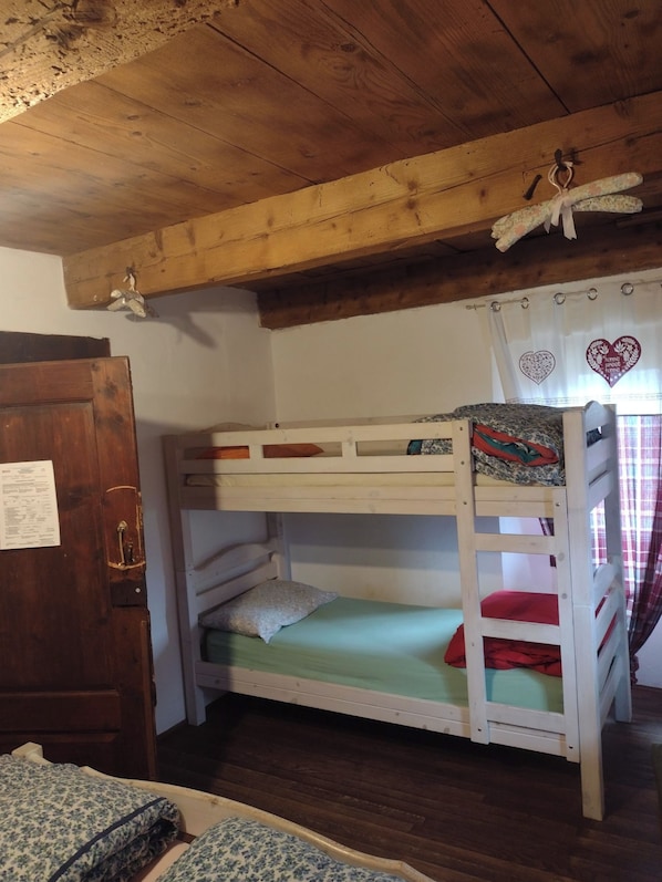 A bunk bed with a wooden ceiling, a door with a paper on it, and a window with heart-shaped curtains. - Rifugio Monte Zeus (Premia)