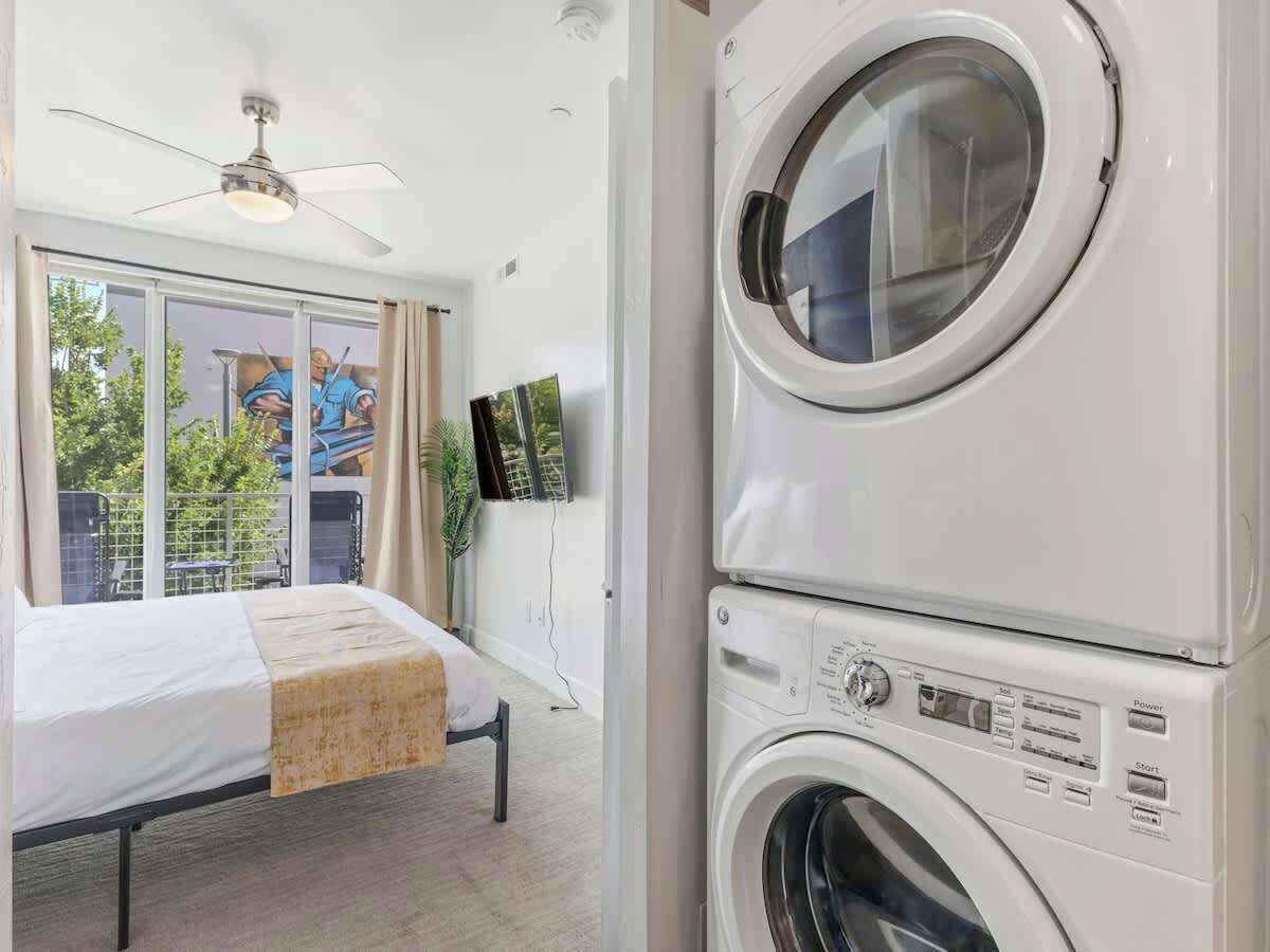 A hotel room with a bed, a ceiling fan, a washing machine, and a TV on the wall.