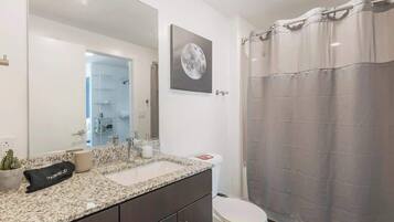 Une salle de bain moderne avec un comptoir en granit, des toilettes blanches, un rideau de douche et un grand miroir.