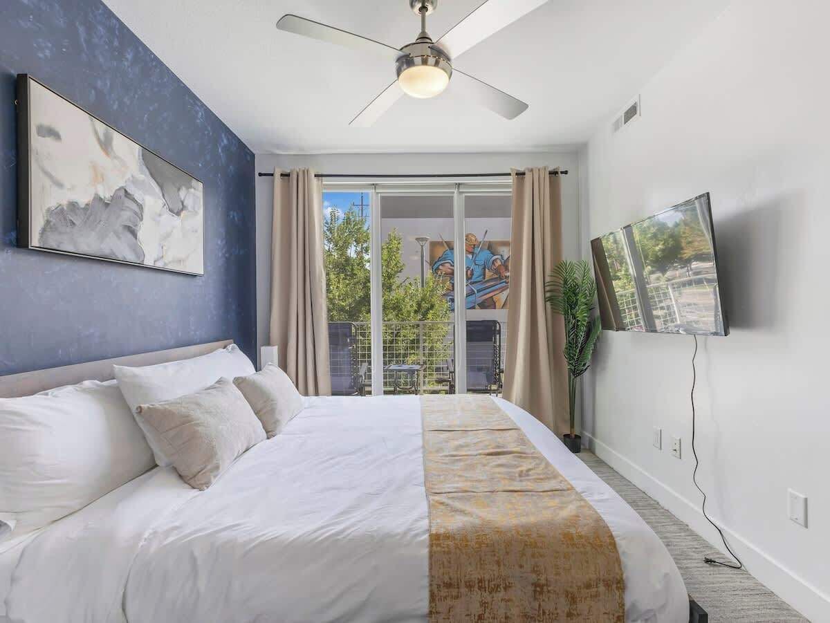 Un dormitorio moderno con una cama grande, un ventilador de techo, un televisor montado en la pared y vistas al exterior a través de una puerta corrediza.