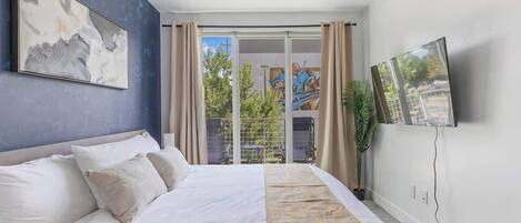 Un dormitorio moderno con una cama grande, un ventilador de techo, un televisor montado en la pared y vistas al exterior a través de una puerta corrediza.