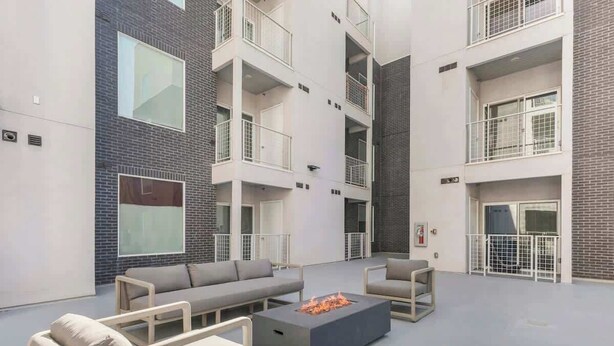 Un espace de détente extérieur moderne, avec un ensemble de canapés gris, une table basse dotée d’un foyer et un balcon avec des balustrades blanches.