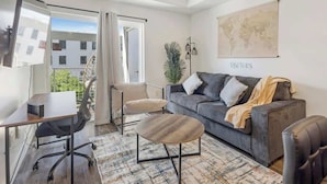 Un salon moderne avec un canapé gris, une table basse en bois, un bureau avec une chaise, un ventilateur de plafond et une carte du monde accrochée au mur.