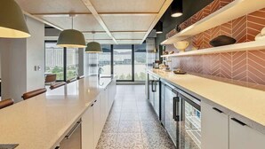 Une cuisine moderne dotée d’un long plan de travail, de luminaires suspendus et offrant une vue sur la ville grâce à de grandes fenêtres.