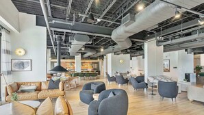 Un intérieur moderne avec un plafond haut, des conduits apparents et différents espaces de détente, notamment des canapés et des fauteuils.