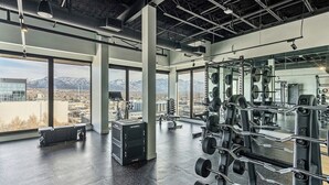 Un gimnasio con equipo de levantamiento de pesas, ventanas amplias y vistas a montañas.