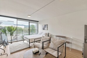 Una habitación de hotel moderna con un balcón grande, un sofá, una cama, una mesita y un televisor.