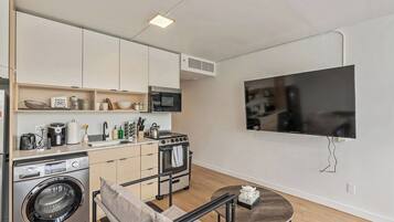 A compact kitchen with a washing machine, oven, microwave, and a flat-screen TV mounted on the wall.