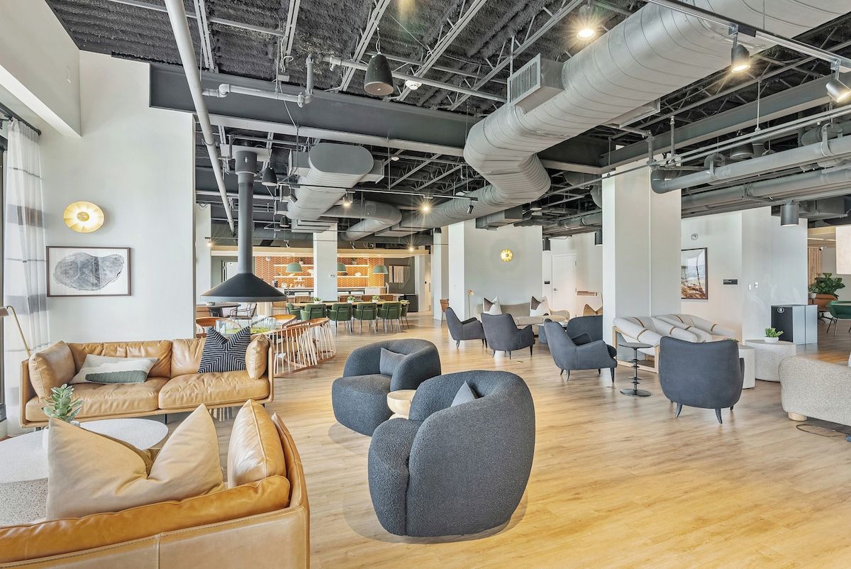 A spacious office with modern furniture, a high ceiling with exposed ductwork, and a mix of seating areas.