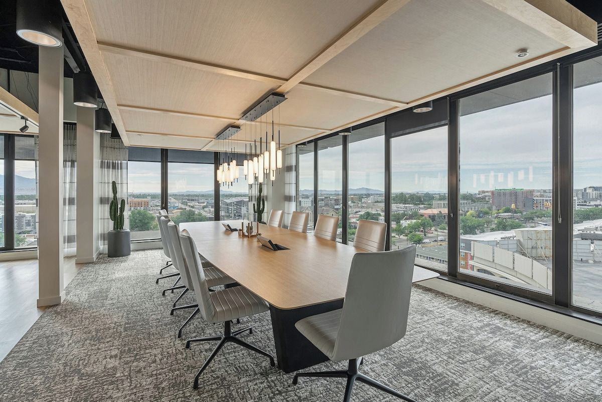 A modern conference room with a large table, chairs, and a city view through large windows.