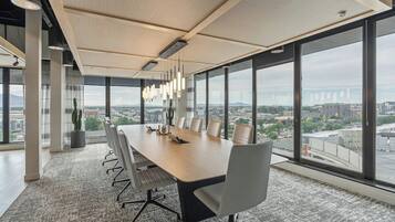 A modern conference room with a large table, chairs, and a city view through large windows.
