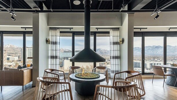 Un área de descanso moderna con una chimenea central, asientos y ventanas amplias que ofrecen vistas a la ciudad.