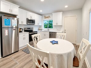 A modern kitchen with white cabinetry, stainless steel appliances, and a dining area with a white table and chairs.