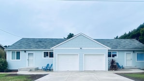 Een gelijkvloers huis met garage, twee ramen aan de voorkant en een klein terras met blauwe stoelen.