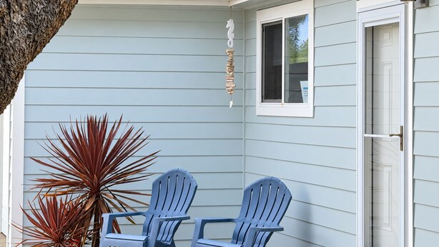 A house with a covered porch, two Adirondack chairs, a potted plant, and a window with a sign. - Salty  Seahorse (Waldport)