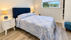 A bedroom with a bed, nightstands, a window, and a view of greenery outside. - Salty  Seahorse (Waldport)