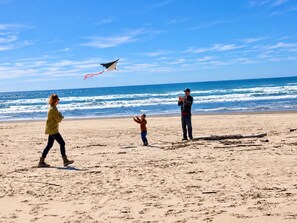 Una spiaggia con una persona che fa volare un aquilone, un'altra persona in piedi accanto a un bambino e una terza persona sullo sfondo.