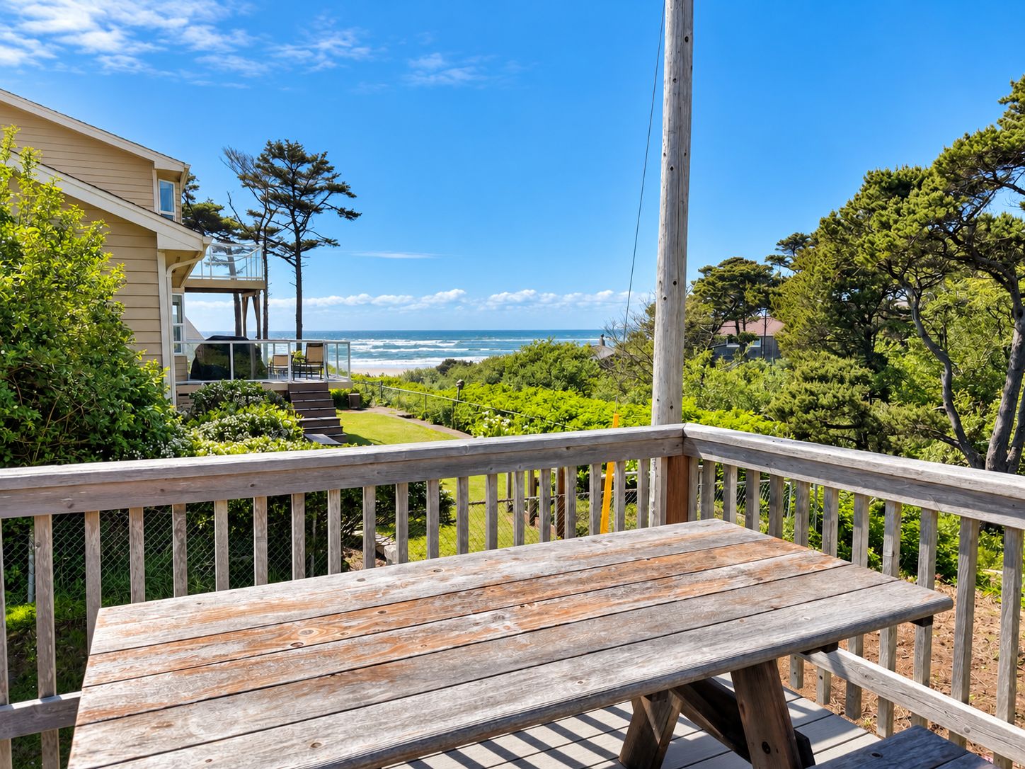 Een houten terras met een bankje met uitzicht op de kustlijn, een huis met balkon, en een heldere lucht.