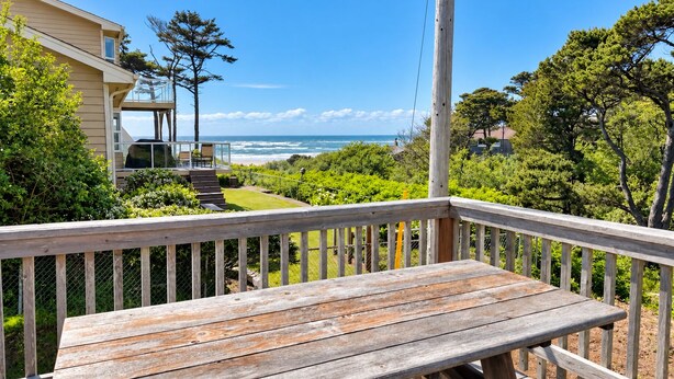 A wooden deck with a bench overlooking a coastal view, a house with a balcony, and a clear sky. - Salty Crab  - Ocean View (Waldport)
