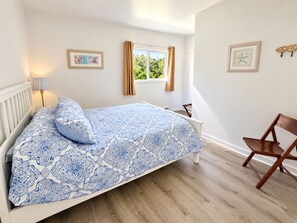 Een slaapkamer met een bed, een stoel, een raam met gordijnen en wanddecoratie.