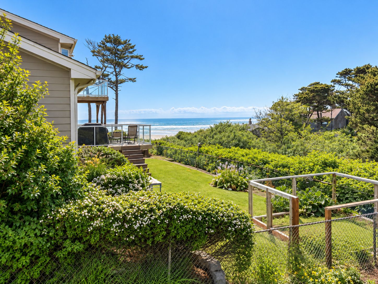 A residential property with a deck overlooking a landscaped garden and a view of the ocean.