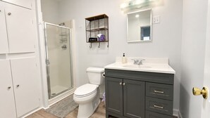 A bathroom with a toilet, a shower, and a vanity with a mirror. - Salty Crab  - Ocean View (Waldport)