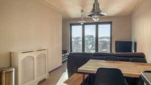 Un soggiorno moderno con un tavolo da pranzo in legno, sedie nere, un divano e un'ampia finestra vista città.