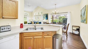 A kitchen with wooden cabinets, a built-in island, a stainless steel sink, and a view to the outdoors. - Townhome Perfectly Located Near Clubhouse (Kissimmee)