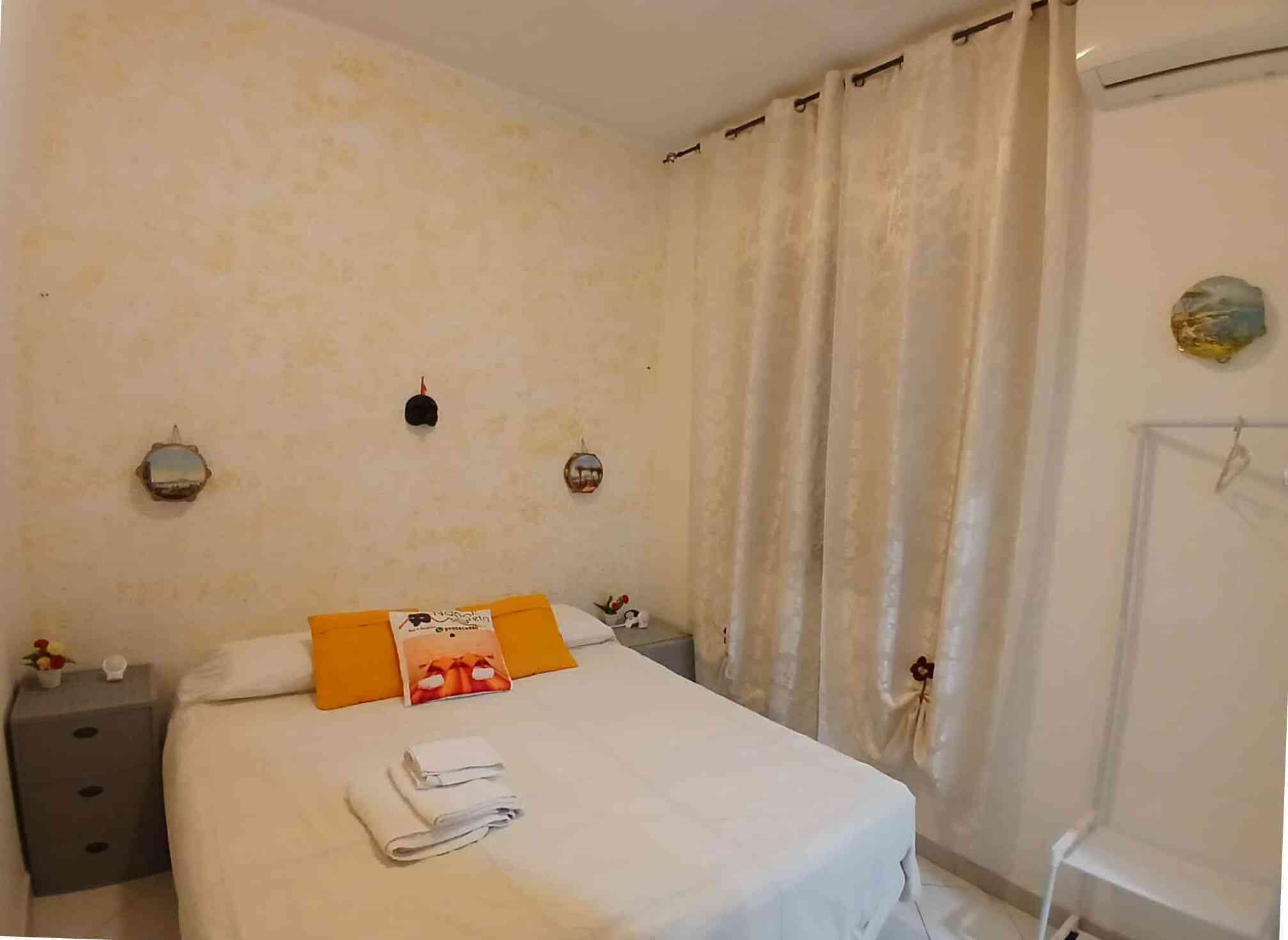 A bedroom with a bed, two bedside tables, a nightstand, a wall-mounted lamp, and a curtain.